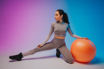 Fashion portrait of young fit and sportive caucasian woman training with fit ball, isolated on gradient background. Perfect body ready for summertime. Beauty, resort, sport concept