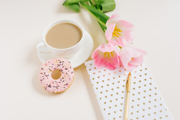 Pink tulips flowers with cup of coffee, notebook and donut on pink background. Blogger concept.