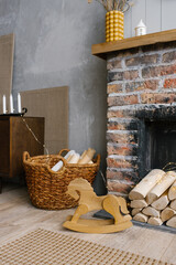Fototapeta na wymiar Red brick fireplace with firewood and a basket of firewood near it, children's wooden toy horse gurney in the living room in the Scandinavian style