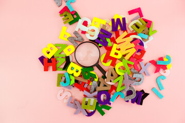 A magnifying glass with the colorful alphabet on pink background. Education concept.