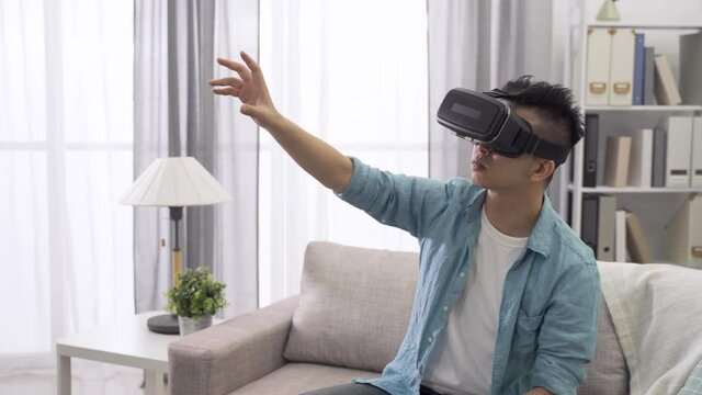 young man playing with VR gadget in living room at home, touching and pointing something in the virtual world.