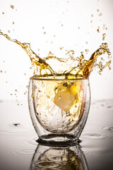 splash in glass with whiskey from falling ice on white background