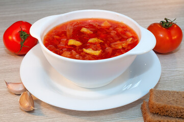 Borscht soup with meat in a white bowl on a wooden table.
