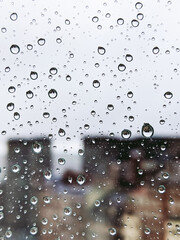 Vertical photo of raindrops on a glass with silhouette of buildings in the background