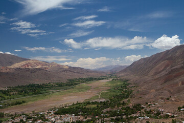 Fototapeta premium Idyllic valley with a beautiful sky. Aerial view of Humahuaca ravine, brown mountains, Andes desert, green valley and Tilcara village in Jujuy, Argentina.