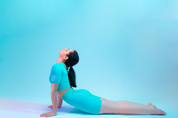 Stretching. Young sportive woman training isolated on gradient studio background in neon light. Modern sport, action, motion, youth concept. Beautiful caucasian woman practicing.