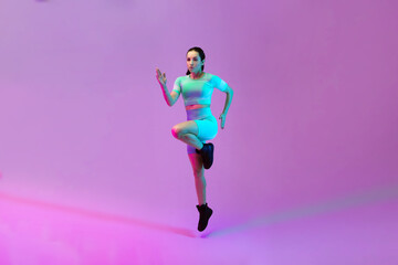 Fototapeta na wymiar Young sportive woman training isolated on gradient studio background in neon light. athletic and graceful. Modern sport, action, motion, youth concept. Beautiful caucasian woman practicing.