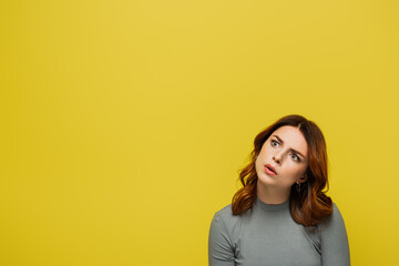 pensive young woman with curly hair looking away isolated on yellow