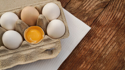 White eggs carton and cracked egg half with yolk top view on wooden background. Easter and healthy food breakfast cooking concept