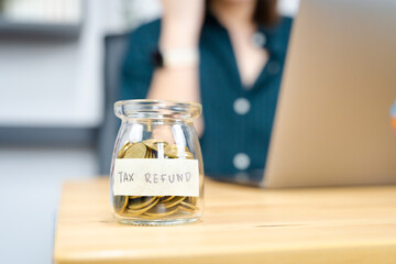 tax refund concept with gold coin in bottle with soft focus woman use laptop background