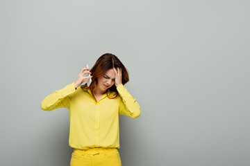 displeased woman frowning and distancing from smartphone on grey