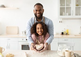 Obraz na płótnie Canvas Happy black man and girl holding dough in heart shape
