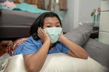 Asian Child wearing a mask and lie on the bed at home. Thai Kid was sick with the flu and rested in the bedroom.