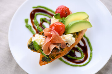 Toasted baguette toast with pesto sauce, a slice of Parma ham, mozzarella, tomato and avocado