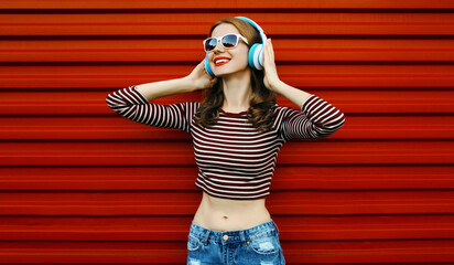 Portrait of happy young woman with wireless headphones listening to music on a red background