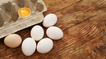 White eggs carton and cracked egg half with yolk top view on wooden background. Easter and healthy food breakfast cooking concept