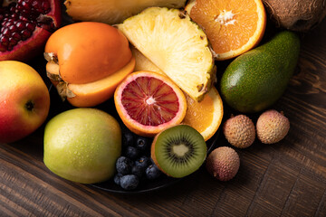 Naklejka na ściany i meble Selection of sliced fresh fruits with kiwis and blood orange on a plate on wooden background