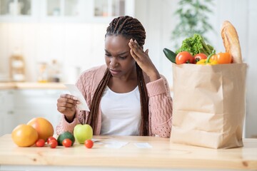 Grocery Expenses. Worry Black Lady Checking Bill In Kitchen After Food Shopping