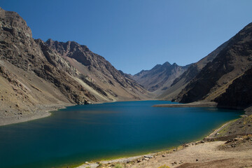 The deep blue color water lake very high in the Andes mountains. View of the Inca Lagoon in Chile, surrounded by rocky mountains and cliffs.