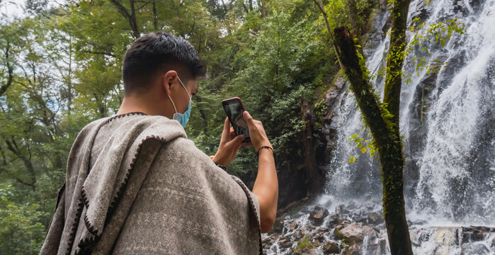 Man with mask taking photos of a waterfall with his cell phone, tourism and covid concept