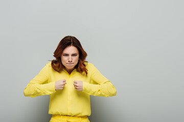 displeased woman with angry grimace and clenched fists looking at camera on grey