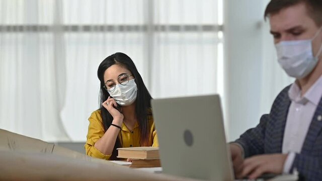 Two employees of company, man woman, put protective masks on faces and work in office observing social distance. Work in office during quarantine compliance with hygiene and health protection measures