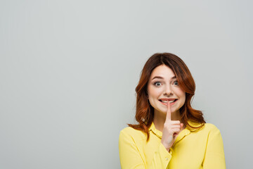 Obraz premium smiling woman with curly hair showing hush gesture isolated on grey