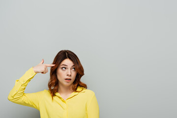 displeased woman showing stupid gesture while looking away on grey