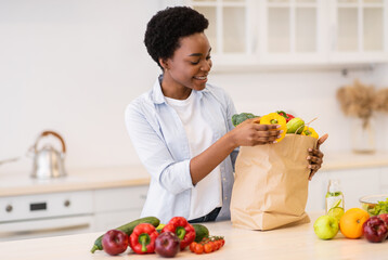 Black Lady Unpacking Grocery Bag After Shopping Standing In Kitchen