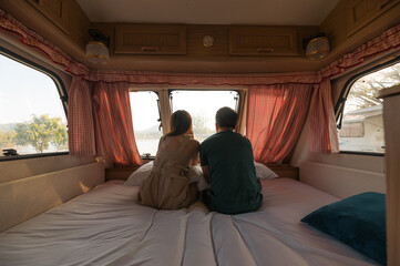 Young couple sitting and taking a view on mattress inside of camper van
