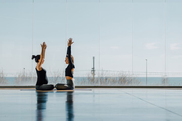 Beautiful full shot of a spacious fitness center with two women doing yoga lotus pose in a...