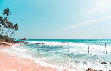 Tropikalna plaża z palmami, niebieski ocean z falami oraz kije rybackie. - obrazy, fototapety, plakaty