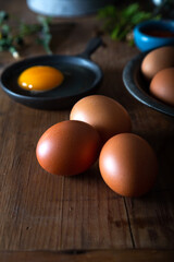 Uncooked fresh chicken eggs and one yolk in the black bowl. Raw chicken eggs on the wooden background. Close up.