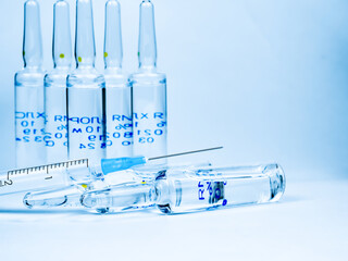 Medical ampoules and syringe on a light-coloured background.