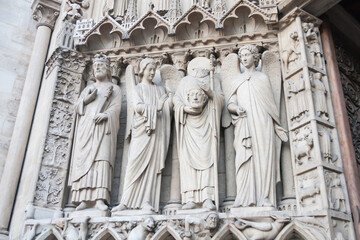Statue of St Denis holding his head with other saints on the exterior facade of Notre Dame de Paris cathedral in Paris, France