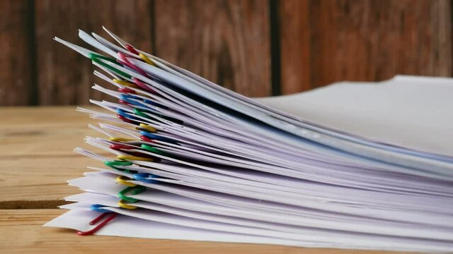 Stack of documents with binder clips wooden table, stop motion animation, closeup
