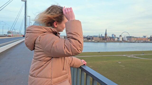 [4k] blonde woman in winter coat standing on bridge putting on sunglasses in Düsseldorf, Germany