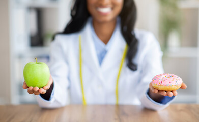 Closeup view of dietitian's hands holding fresh apple and donut at table in medical office. Dieting...