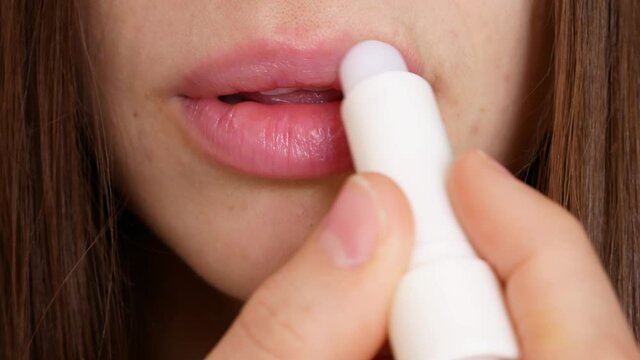 Close-up of the lips of a pretty young woman smearing them with lip balm