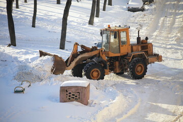 One yellow powerful wheeled bulldozer tractor removes a snow with scraper shovel blade snowplow on...