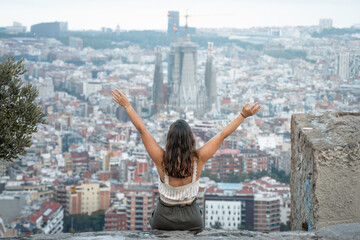Fototapeta premium Free traveler woman raises her arms with a beautiful view of the city of Barcelona, Spain 