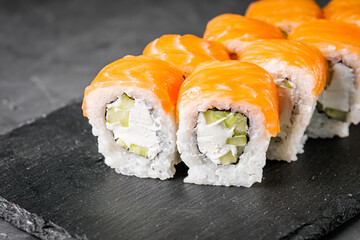 appetizing philadelphia sushi roll with salmon and cucumber on a black stone plate