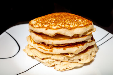 stack of pancakes on a plate against a black background
