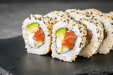 appetizing california sushi roll with cheese avocado cucumber and salmon in sesame seeds on a black stone plate