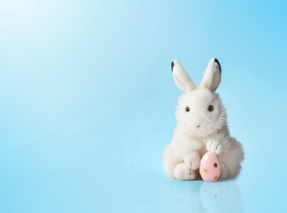Easter bunny rabbit with pink painted egg on blue background. Easter holiday concept.
