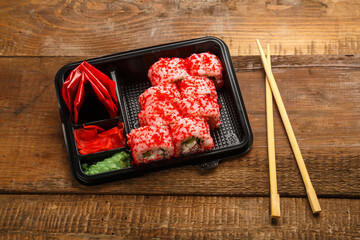 Roll with shrimp, cucumber, wasabi cream cheese and tobiko caviar and sticks in a box with ginger on a wooden background next to sticks. copy space