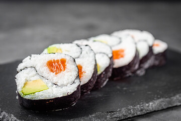 appetizing sushi roll futomaki yin yang with salmon and avocado on a black stone plate