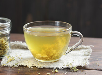 Meadowsweet floral herbal tea in glass cup with dried herb in a jar nearby on the wooden rustic table, closeup, copy space, natural medicine and healthy herbal tea concept