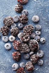Frozen blueberries and blackberries with crushed ice over dark blue concrete background. Overhead view, close up. Healthy food background