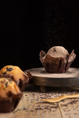 View of chocolate muffins, with selective focus, on wooden table with chocolate shavings and sugar falling, in vertical, with copy space